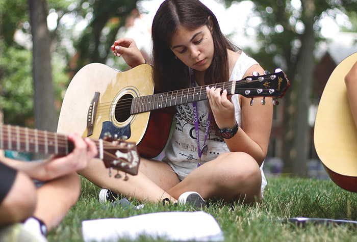 A teenage girl plays guitar in the grass